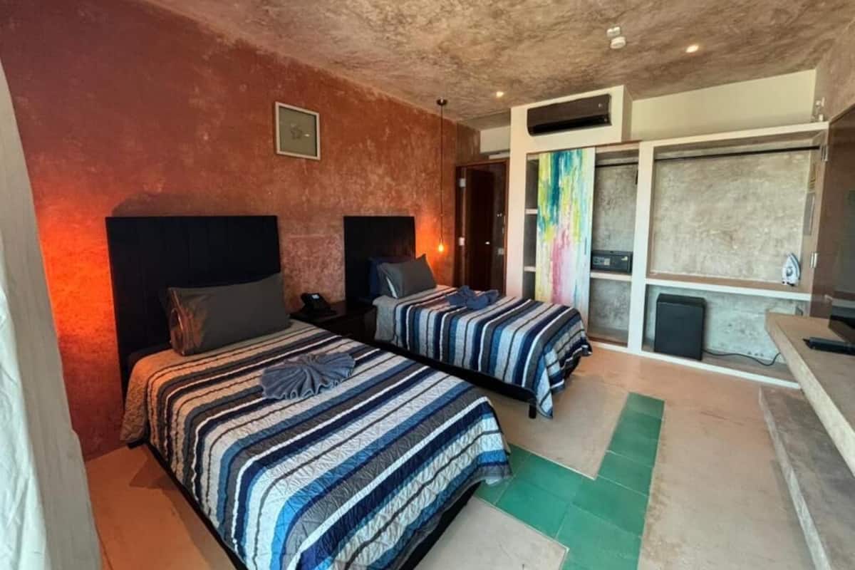 A room with two beds, a large window with a colorful view, and a kitchenette area.