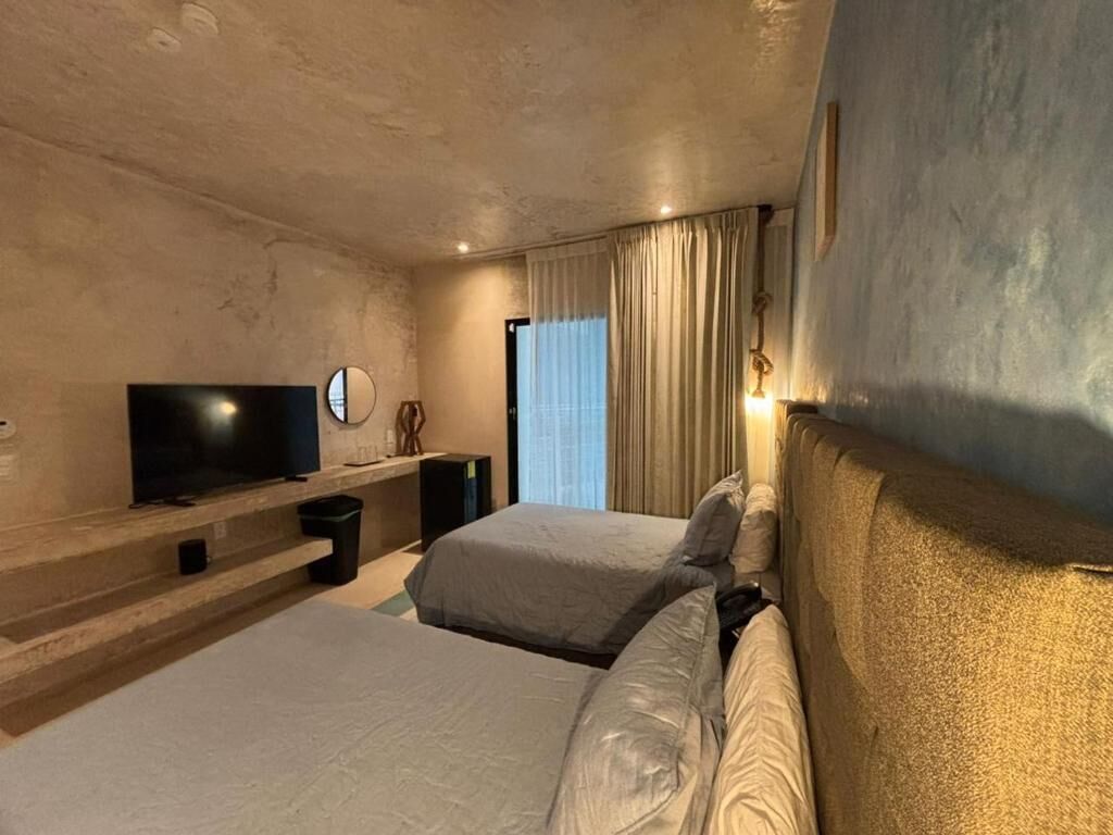 Habitación de hotel con dos camas, televisión de pantalla plana, mesita de noche y un gran ventanal con cortinas.