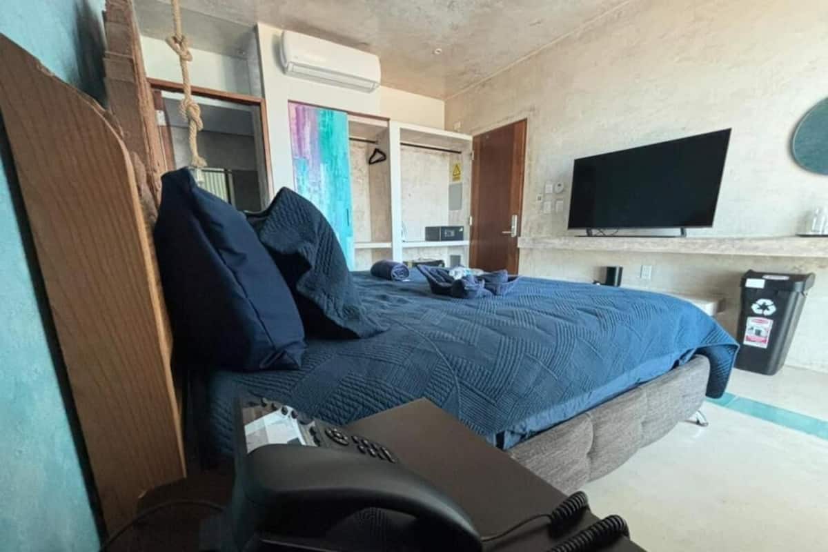 A hotel room with a bed, a desk with a telephone, a TV mounted on the wall, and a trash bin.