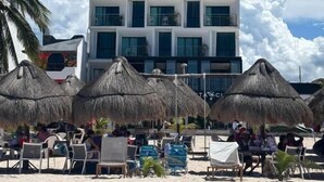 A multi-story hotel with a beachside view, featuring thatched umbrellas and beach chairs. - Simple & Luxury (Progreso)