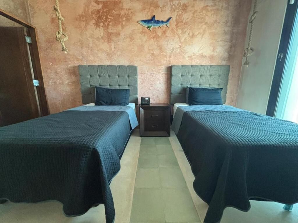 Una stanza con due letti, un piccolo comodino e una decorazione a forma di pesce appesa al muro.