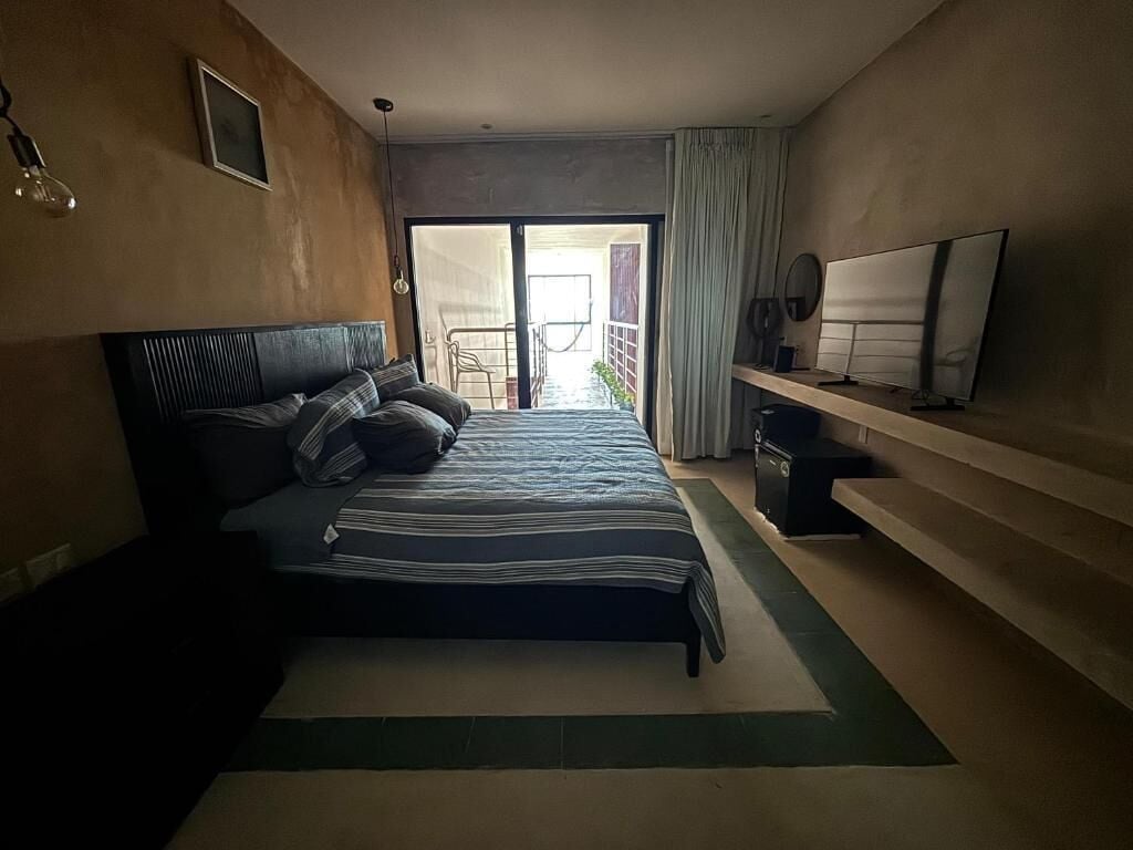 A bedroom with a bed, a TV, a desk, and a view of the outside.