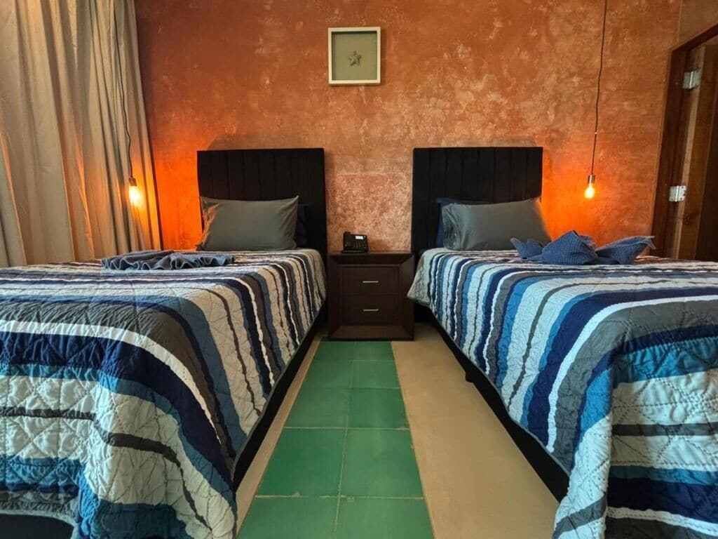 Une chambre d’hôtel avec deux lits, un sol vert, une porte en bois et une horloge murale.