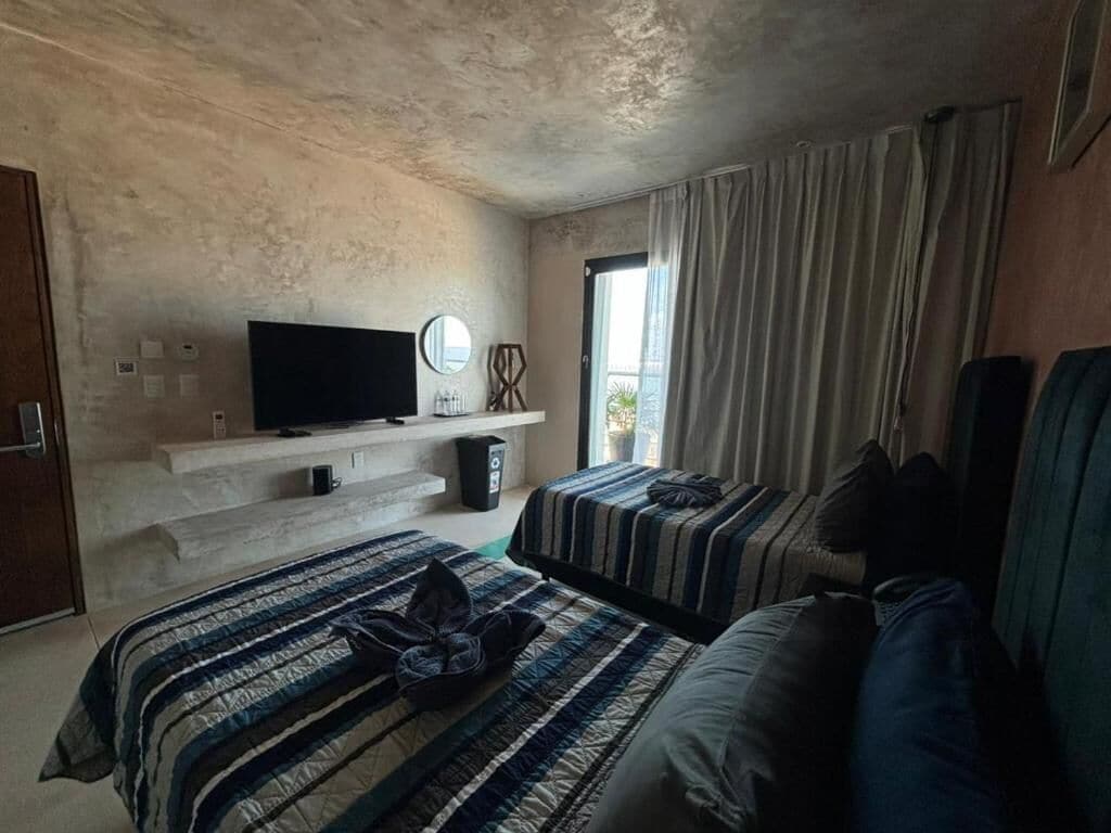 Habitación de hotel con dos camas, televisión, una mesita y ventana con cortinas.