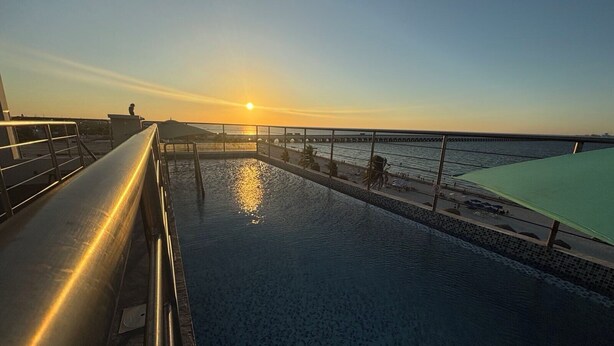 A pool with a sun reflecting on the water, a railing, and a view of the sunset over the water. - Simple & Luxury (Progreso)