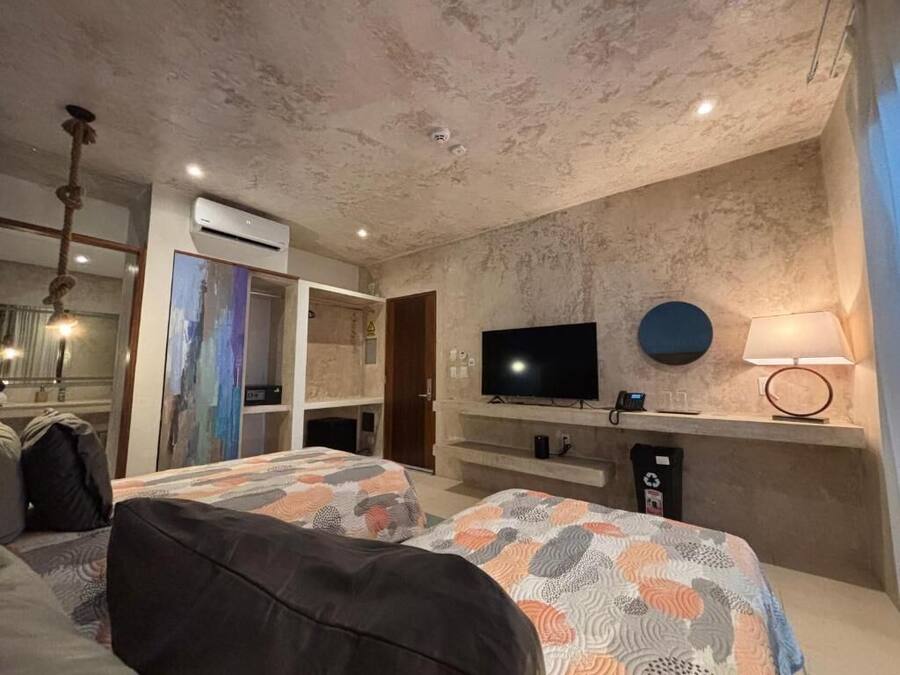 Habitación de hotel con dos camas, un televisor de pantalla plana, aire acondicionado instalado en la pared y una lámpara.