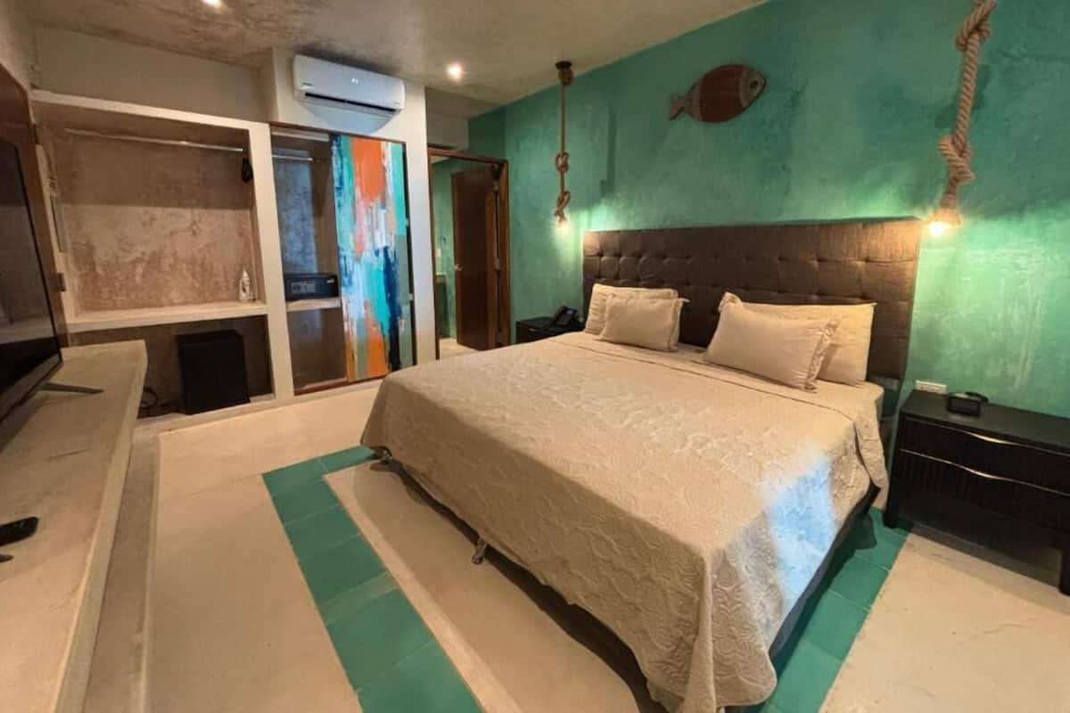 A bedroom with a large bed, a wooden headboard, a nightstand, and a wall-mounted air conditioner.