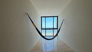 A hallway with a hammock hanging from the ceiling, a large window at the end, and a polished floor. - Simple & Luxury (Progreso)