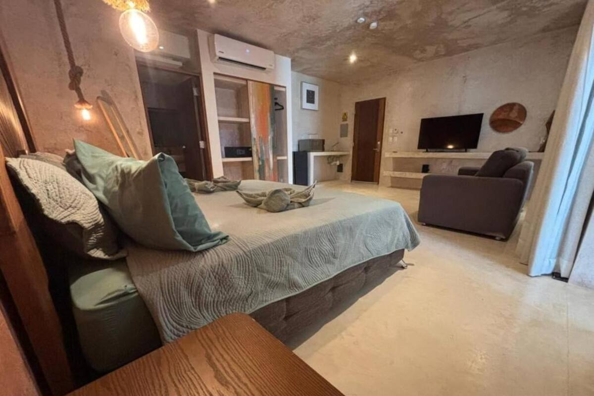 A cozy bedroom with a bed, a wooden bench, a TV, and a sofa.