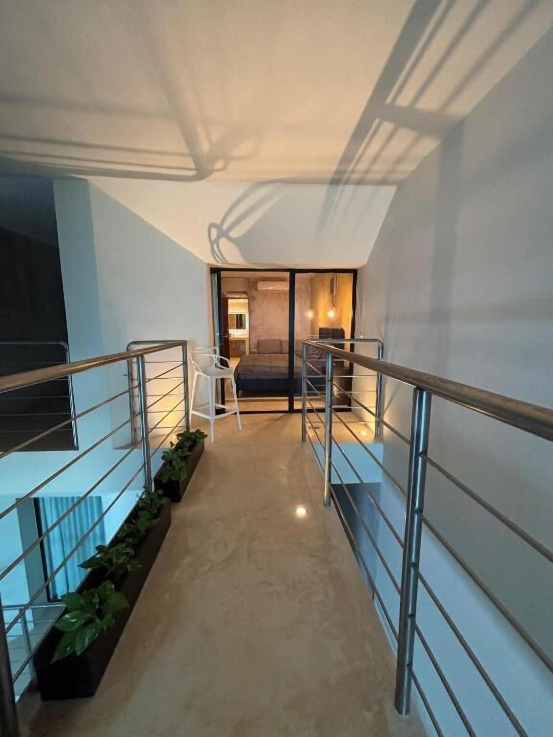 Un interior modern amb una escala, baranes metàl·liques i una zona d'estar amb taula i cadires.