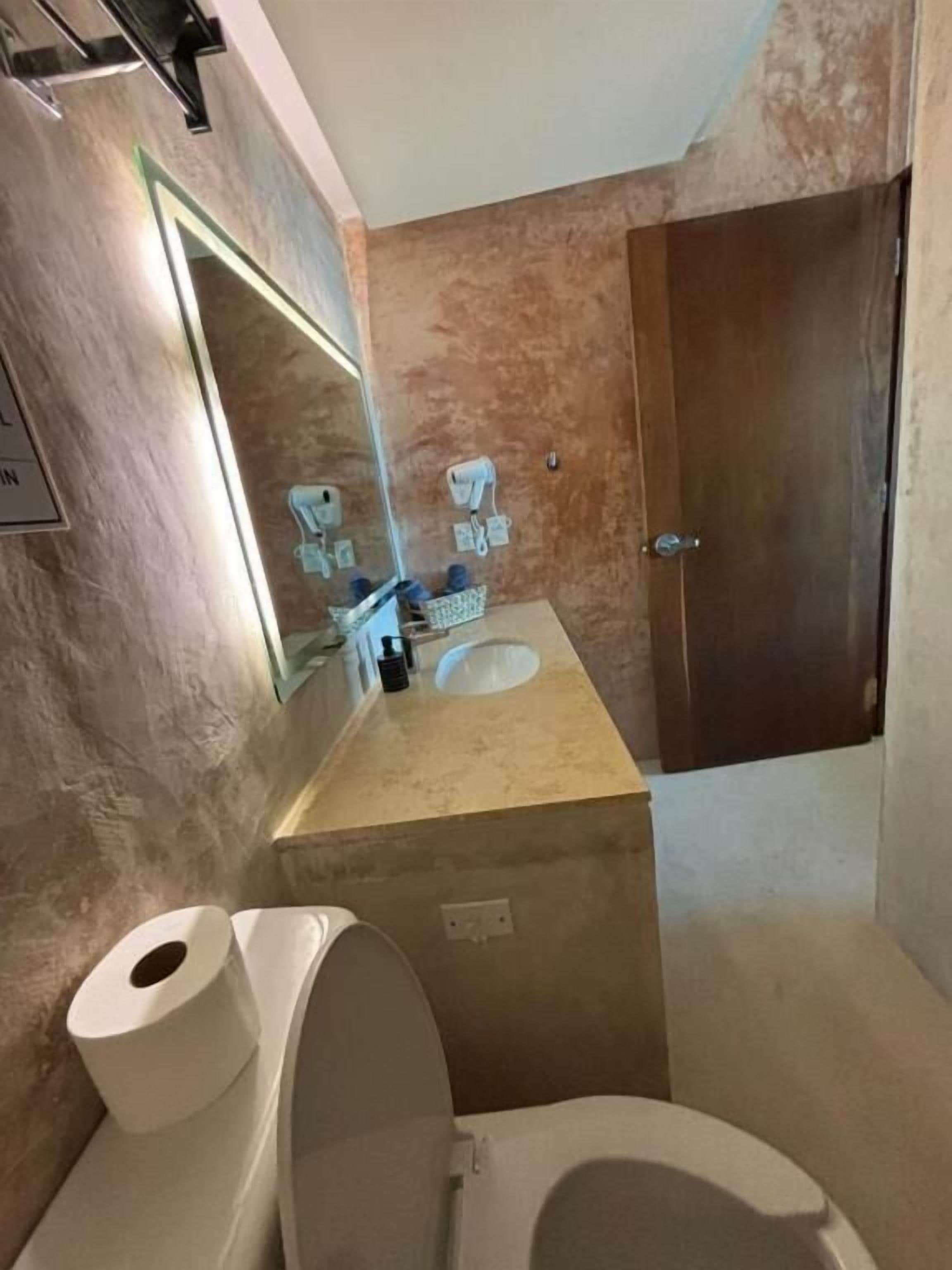 Een badkamer met een marmeren wand, een wastafel, een toilet en een spiegel.