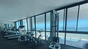 A gym with various exercise equipment and large windows offering a view of the sea. - Simple & Luxury (Progreso)