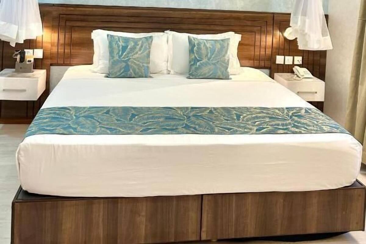 Een hotelkamer met een bed, nachtkastjes, een houten hoofdbord en een blauwe wand met structuur.