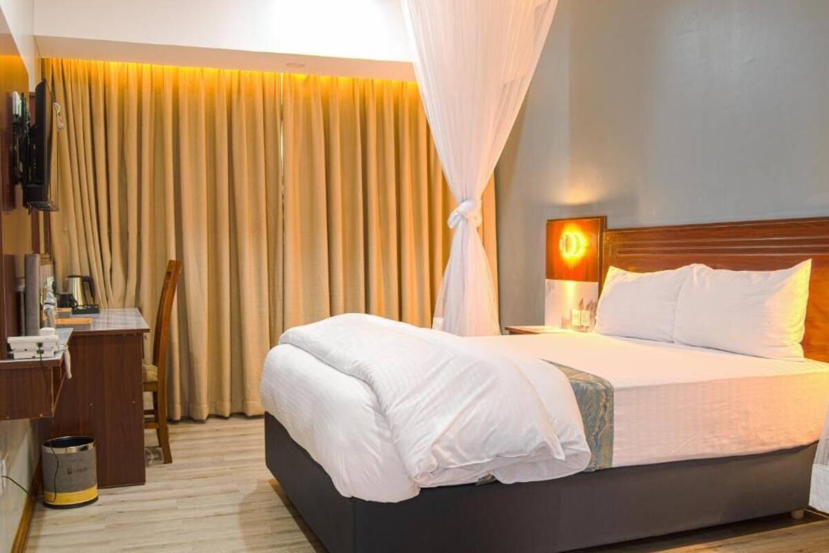 Een hotelkamer met een bed, een bureau, een stoel, een televisie en gordijnen.