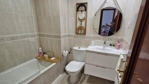Een moderne badkamer met een badkuip, toilet, wastafel en badkamerkast.