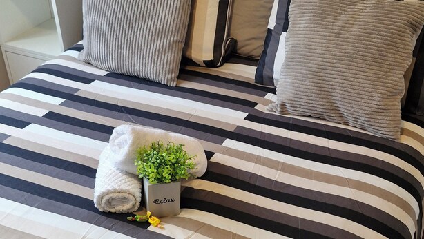Een bed met gestreepte lakens, een plantje en een handdoek.