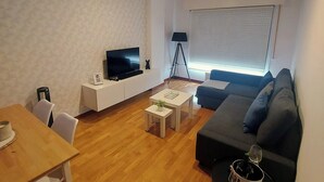 Een moderne woonkamer met een flatscreen televisie, een bank, een eettafel en een lamp.