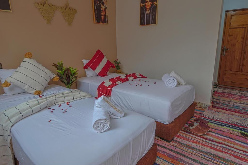 A hotel room with three beds, each with white linens and red accents, a colorful striped carpet, and a wooden door.