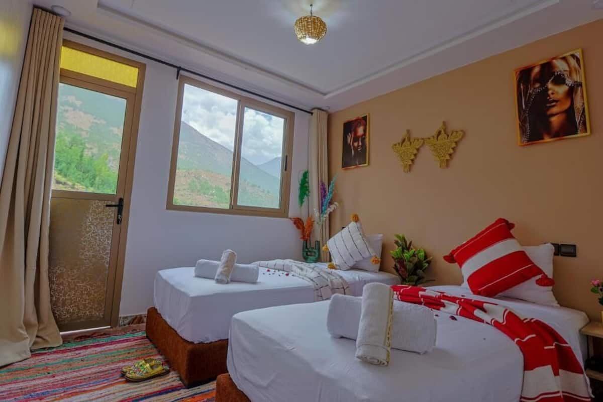 A hotel room with two beds, a sliding glass door to a balcony, and a view of the mountains.