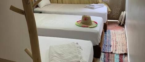 Una habitación pequeña y acogedora con dos camas individuales, una silla de madera, una mesita y una ventana con cortinas.