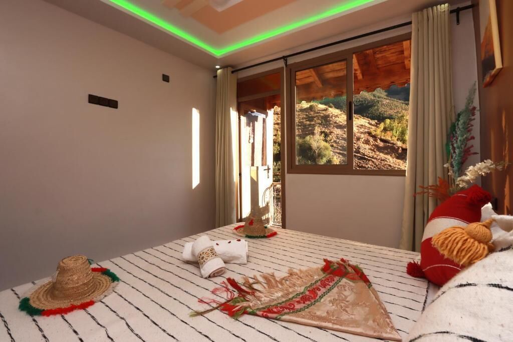 Una habitación con un ventanal grande, una cama, un sombrero y un tapete decorativo.