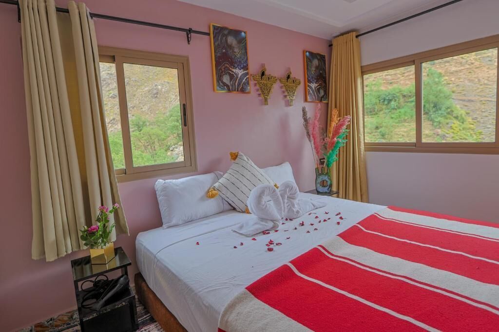 A neatly made bed with a red and white striped blanket, a bouquet of flowers, and a vase on a bedside table.