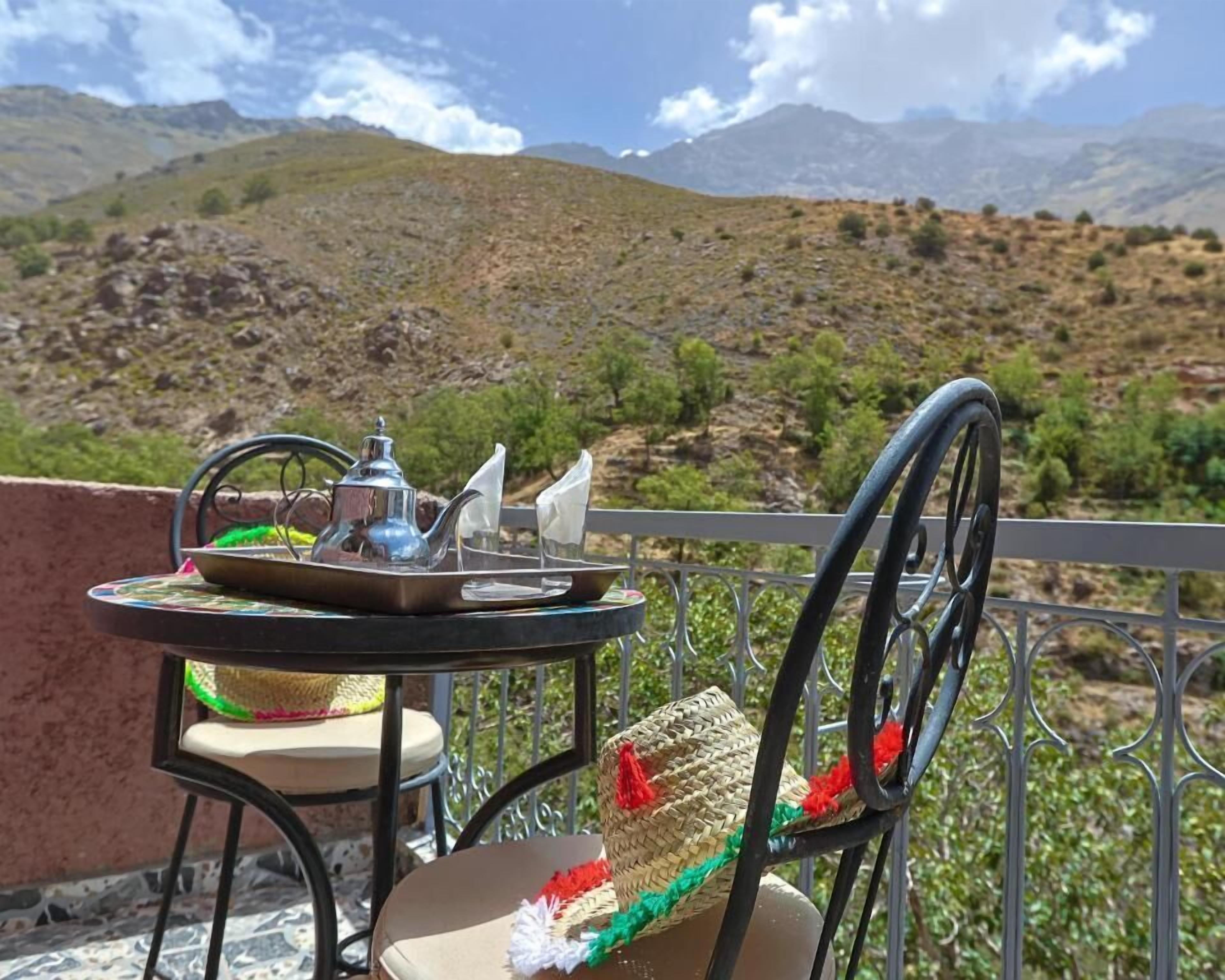 A table with a teapot and cups on a balcony with a view of mountains.