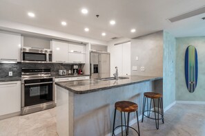 A modern kitchen with stainless steel appliances, a marble countertop, and a bar area with stools. - The Netherland R5B on OceanDr (Miami Beach)