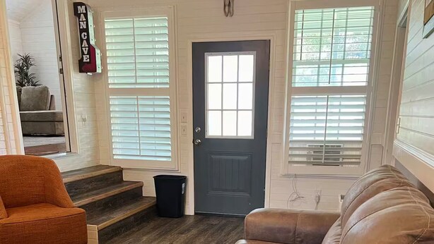 A living room with a brown leather sofa, an orange armchair, and a wooden floor. There is a black trash bin and a door with a bull skull decoration. - Family Friendly home down from the lake, just minutes to a dock and downtown! (Guntersville)