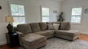 A living room with a sectional sofa, a patterned rug, and a lamp on a side table. - Family Friendly home down from the lake, just minutes to a dock and downtown! (Guntersville)
