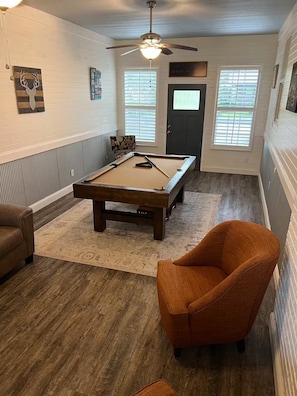 Une pièce avec une table de billard, un ventilateur de plafond, un canapé en cuir marron et un tapis à motifs.