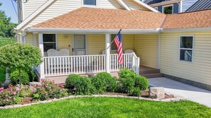 A single-story house with a porch, a flag, and a well-maintained garden. - Lakefront sunsets, dock fishing & cozy fire · 20 min to Mad River (Belle Center)