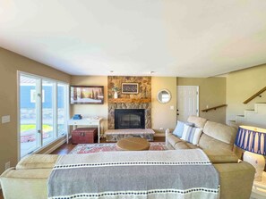 A living room with a fireplace, a sofa, a coffee table, and a view through large glass doors.