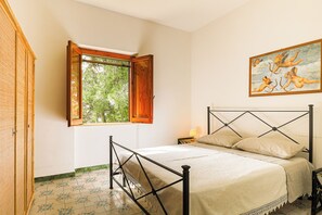 Ein Schlafzimmer mit Bett, einem Fenster mit Blick auf Bäume, einem Bild an der Wand und einem hölzernen Kleiderschrank.