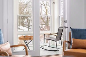 Een kamer met een schuifglazen deur die uitkomt op een balkon met twee stoelen en een kleine tafel.