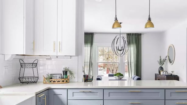 A modern kitchen with white cabinets, a grey countertop, and gold handles. There are two pendant lights, a window with green curtains, and a small plant on the counter. - Sleeps 12, Firepit, near Downtown/SU (Syracuse)