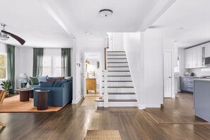 Een modern interieur met een trap naar een tweede verdieping, een zithoek met een blauwe bank, houten vloeren en een keuken met witte kasten.