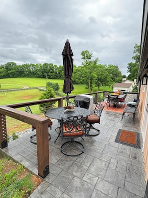 A patio with a round table and chairs, a grill, and a view of a green field.