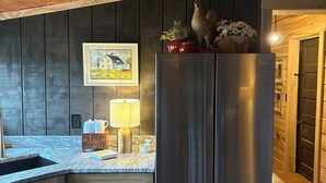 A kitchen with a stainless steel refrigerator, wooden cabinets, a marble countertop, and a framed picture on the wall. - Working Horse Ranch Retreat – 2 Bedrooms, Fire Pit, 20 Min to Downtown Nashville (Goodlettsville)