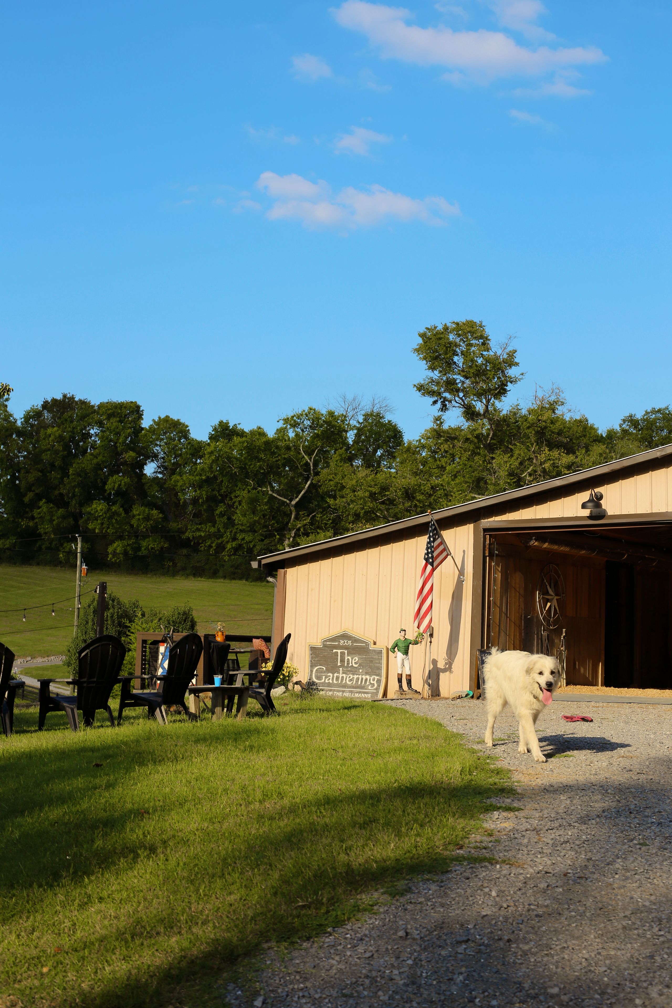 A rustic barn with an American flag, a sign reading 'The Gathering,' and a dog in front.
