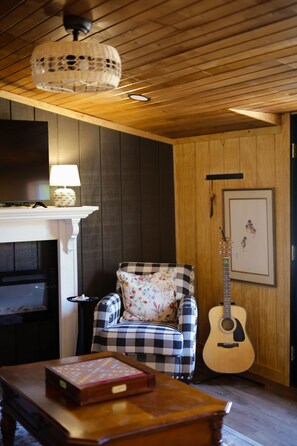 A cozy room with a fireplace, a checkered armchair, a guitar, and a wooden coffee table. - The Gathering Stables - Country charm on a horse farm, minutes from Nashville (Goodlettsville)