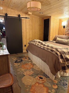 A wooden-paneled room with a bed, a chair, and a door.