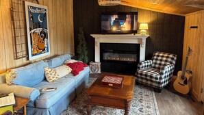 A cozy living room with a blue sofa, a checkered armchair, a wooden coffee table, a fireplace, and a guitar. - Working Horse Ranch Retreat – 2 Bedrooms, Fire Pit, 20 Min to Downtown Nashville (Goodlettsville)