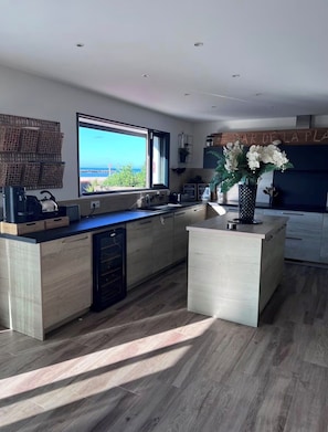 A modern kitchen with a large island, wooden cabinetry, and a view of the sea through a large window. - Ma vie là - House on the beach (Valras-Plage)