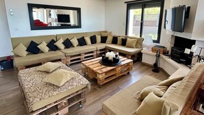 A modern living room with a sectional sofa, a wooden coffee table, and a TV mounted on the wall. - Ma vie là - House on the beach (Valras-Plage)