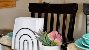 Un comedor con una mesa de madera, sillas, un jarrón blanco con flores y un cartel que dice 'WELCOME' en la pared.