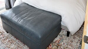 Un dormitorio con cama, mesita de noche, lámpara, ventana con persianas y una alfombra estampada.