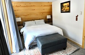 A bedroom with a wooden headboard, a bed with white linens, a bedside table with a lamp, a rug, and a framed picture on the wall. - Delightful 3-bedroom chalet in charming Salida perfect for getaway (Salida)