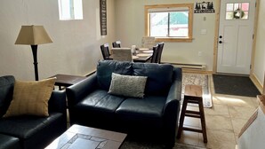 Una sala de estar con un sofá de cuero negro, una mesita de centro, una lámpara y un comedor con mesa y sillas.