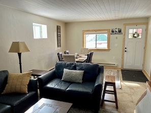 A living room with a black leather sofa, a small coffee table, a lamp, and a dining area with a table and chairs.